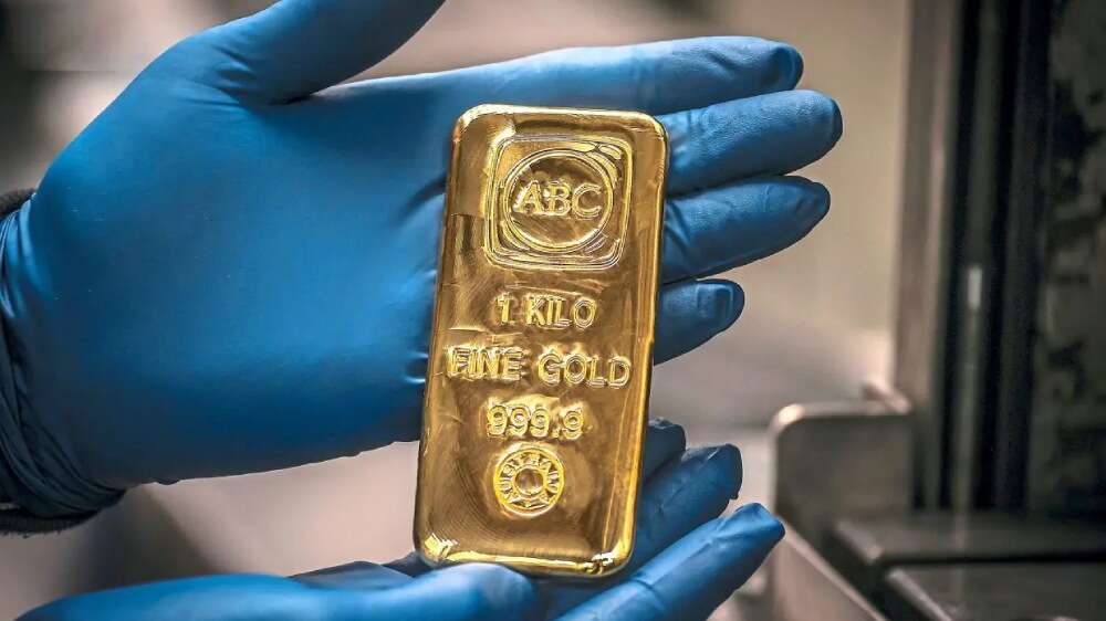 دستانی با دستکش آبی که یک شمش طلای ۱ کیلوگرمی خالص با مهر ABC را نگه داشتهاند