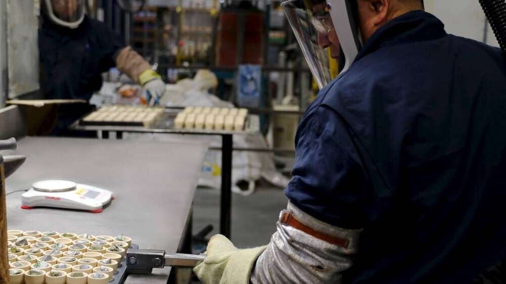 کارگران با تجهیزات ایمنی، بوتههای حاوی نمونه طلا را در کارگاه ری گیری، برای عیارسنجی آماده میکنند