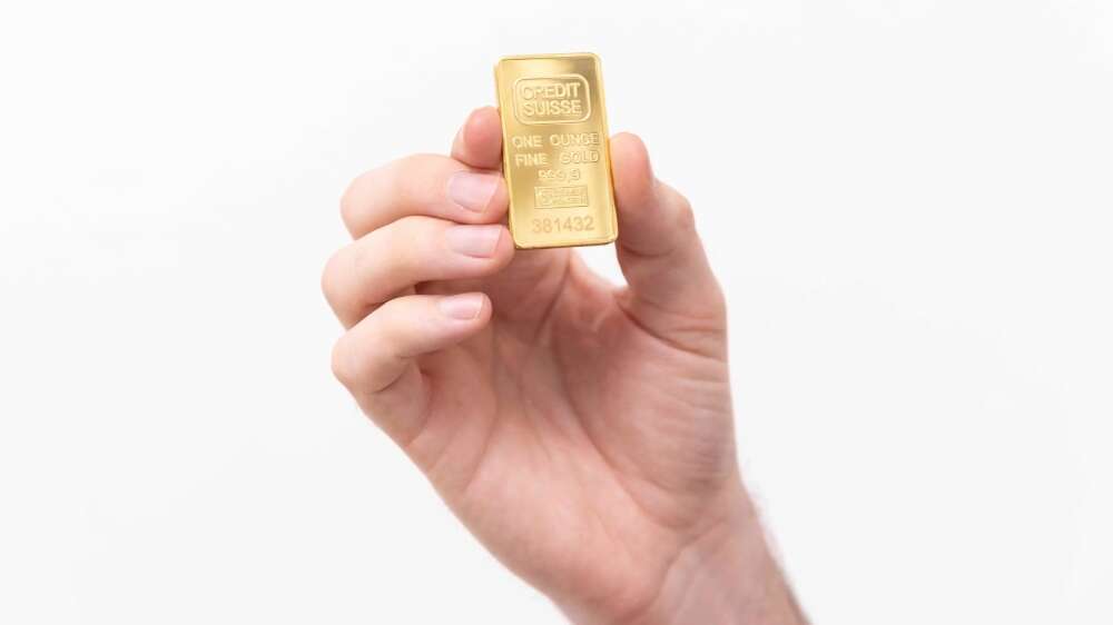 دستی که یک شمش طلای کوچک یک اونسی از برند کردیت سوئیس را در دست گرفته است