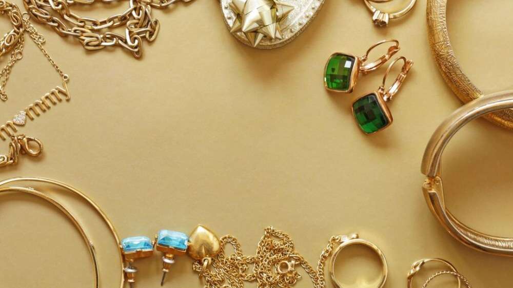 مجموعهای از جواهرات طلایی، شامل گردنبند، دستبند و گوشوارههای نگیندار روی پسزمینه طلایی