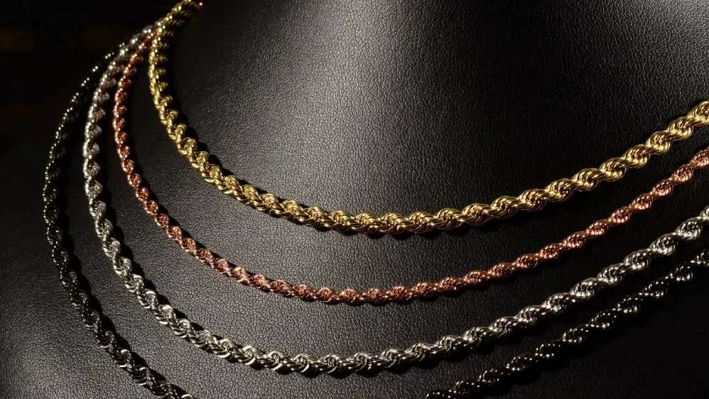 چهار زنجیر طلای مشکی، سفید، رزگلد و زرد که کنار هم روی سطحی تیره قرار دارند