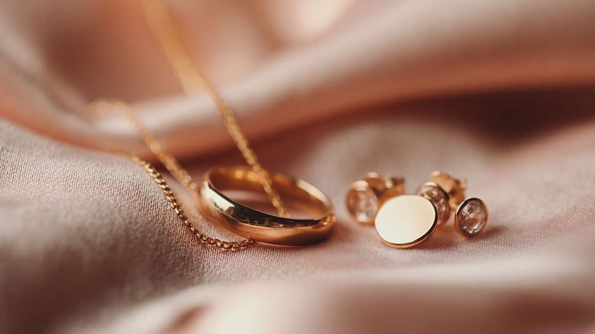 نمای نزدیک از حلقه و گوشواره‌های طلایی براق روی پارچه‌ای ابریشمی و نرم با نور گرم و لطیف