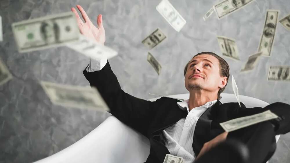 مردی با کت و شلوار غرق در ثروت و آسودگی در حالی که باران اسکناس روی سرش میبارد