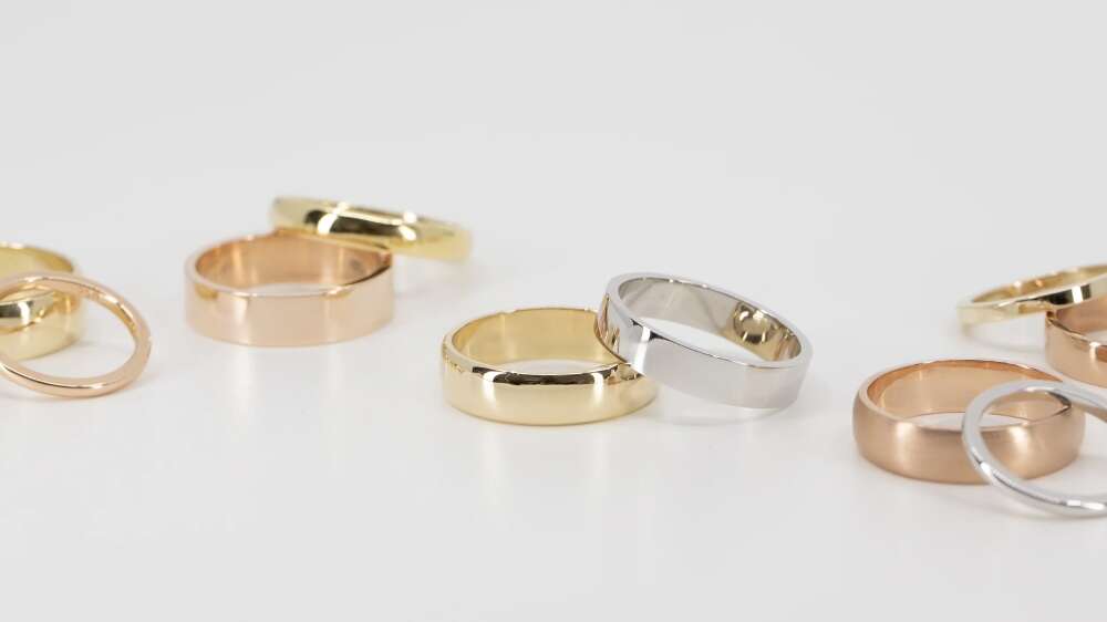 حلقه‌های ساده طلا در رنگ‌های زرد، سفید و رزگلد به‌صورت پراکنده روی یک سطح سفید