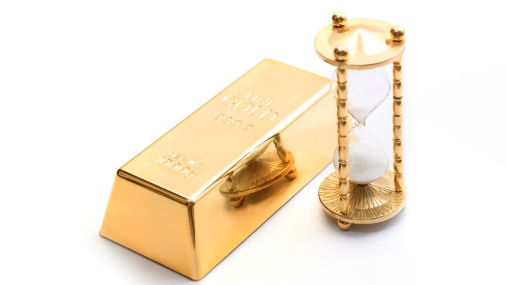 شمش طلا کنار ساعت شنی طلایی که نماد سرمایه گذاری است