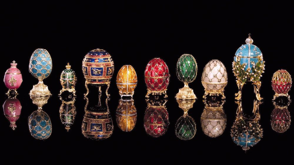 ردیفی از دوازده تخم‌مرغ فابرژه گران‌بها و رنگارنگ روی پایه‌های طلایی با پس‌زمینه سیاه