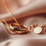 نمای نزدیک از حلقه و گوشواره‌های طلایی براق روی پارچه‌ای ابریشمی و نرم با نور گرم و لطیف